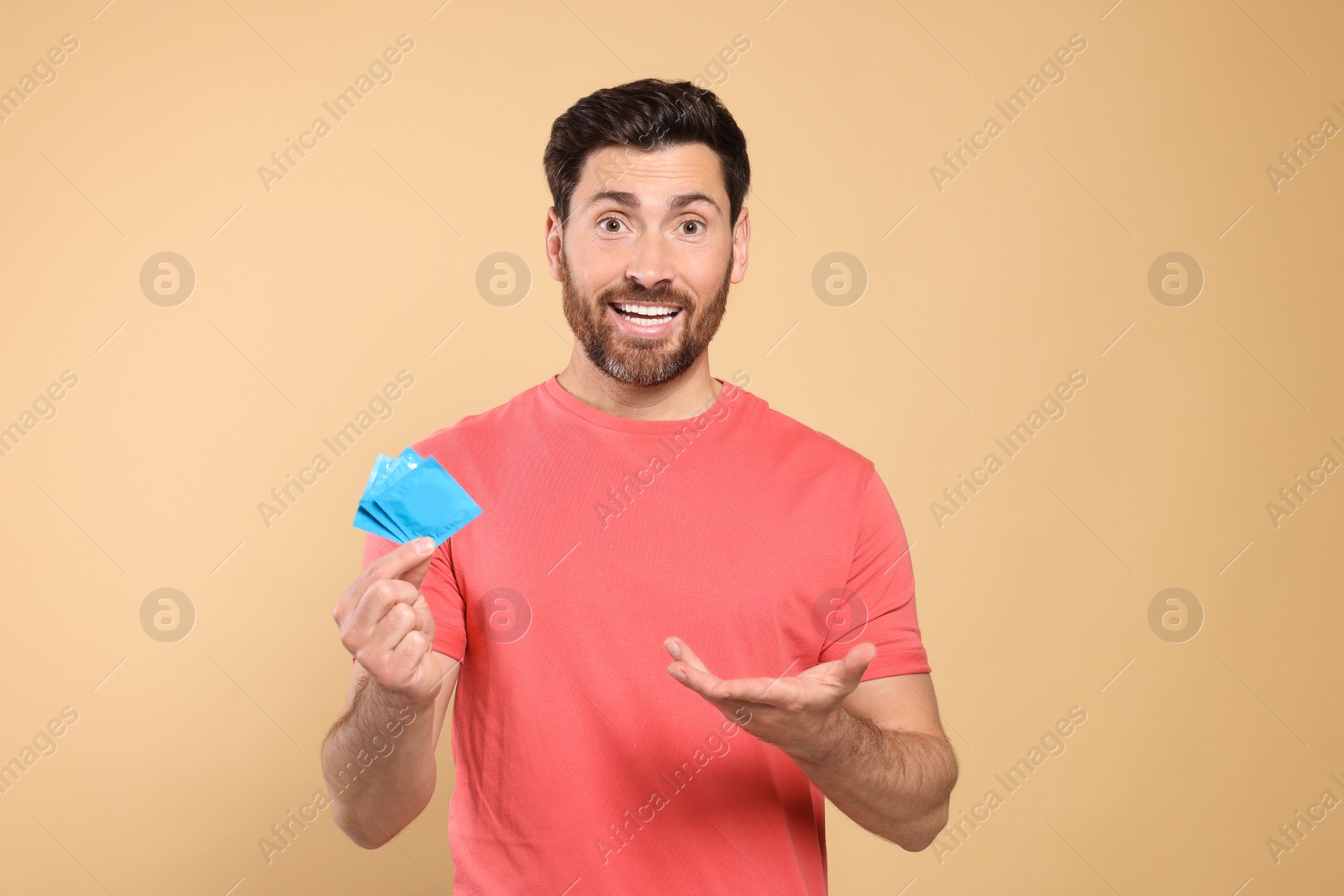 Photo of Emotional man holding condoms on beige background. Safe sex