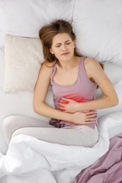 Image of Woman suffering from abdominal pain in bed, top view
