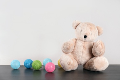 Photo of Adorable teddy bear and colorful garland on table against light background, space for text. Child room elements