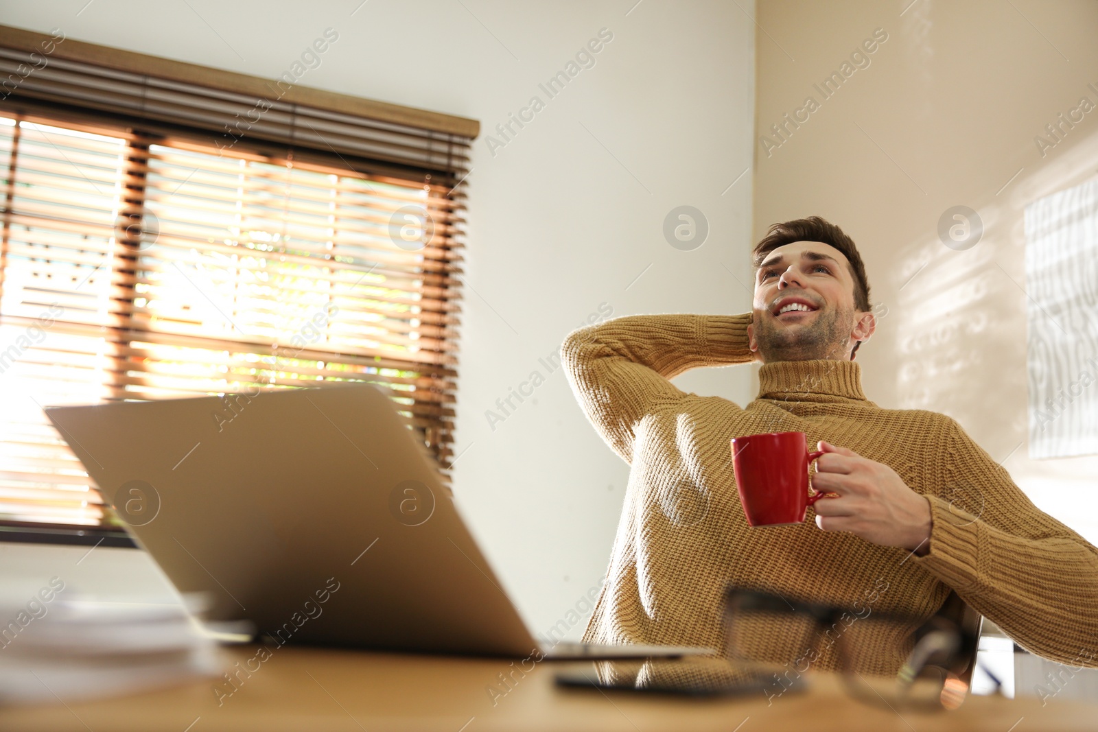 Photo of Young man with cup of drink relaxing at workplace