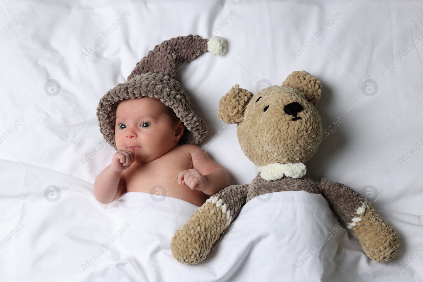 Photo of Cute little baby with toy bear lying under blanket in bed, top view