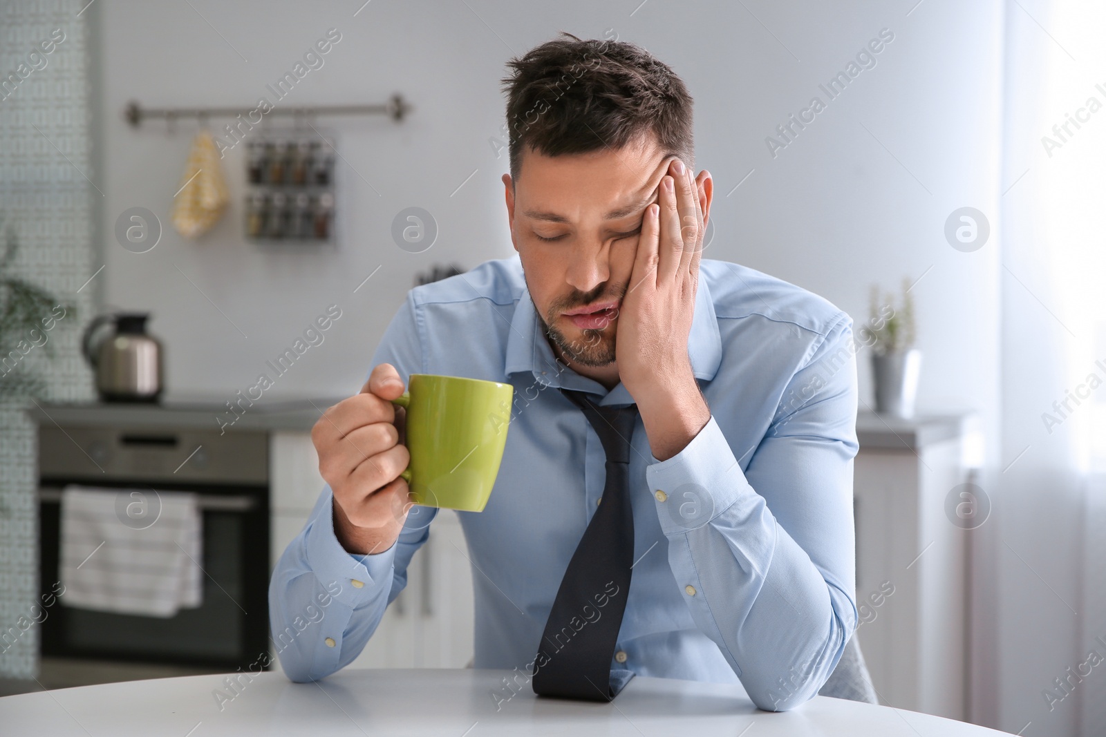 Photo of Sleepy man with cup of drink at home in morning