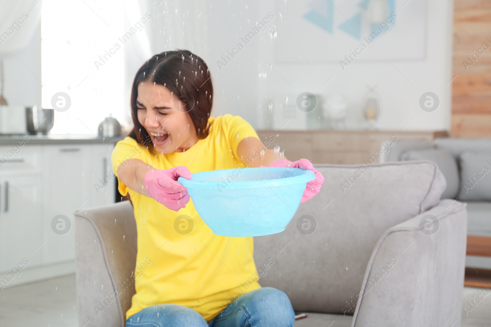 Photo of Woman collecting water leaking from ceiling at home. Time to call plumber