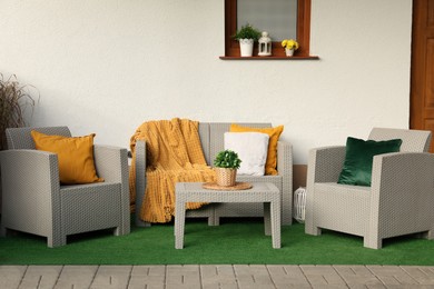 Photo of Beautiful rattan garden furniture, soft pillows, blanket and houseplant near white wall