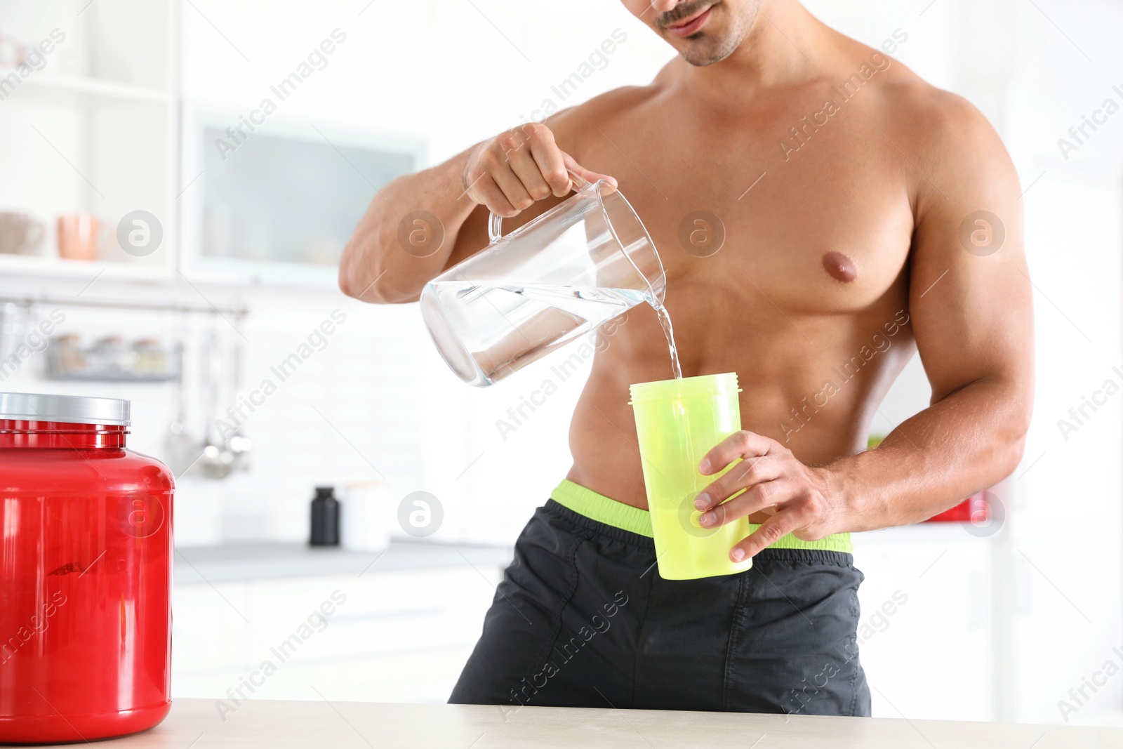 Photo of Young shirtless athletic man preparing protein shake in kitchen, closeup view