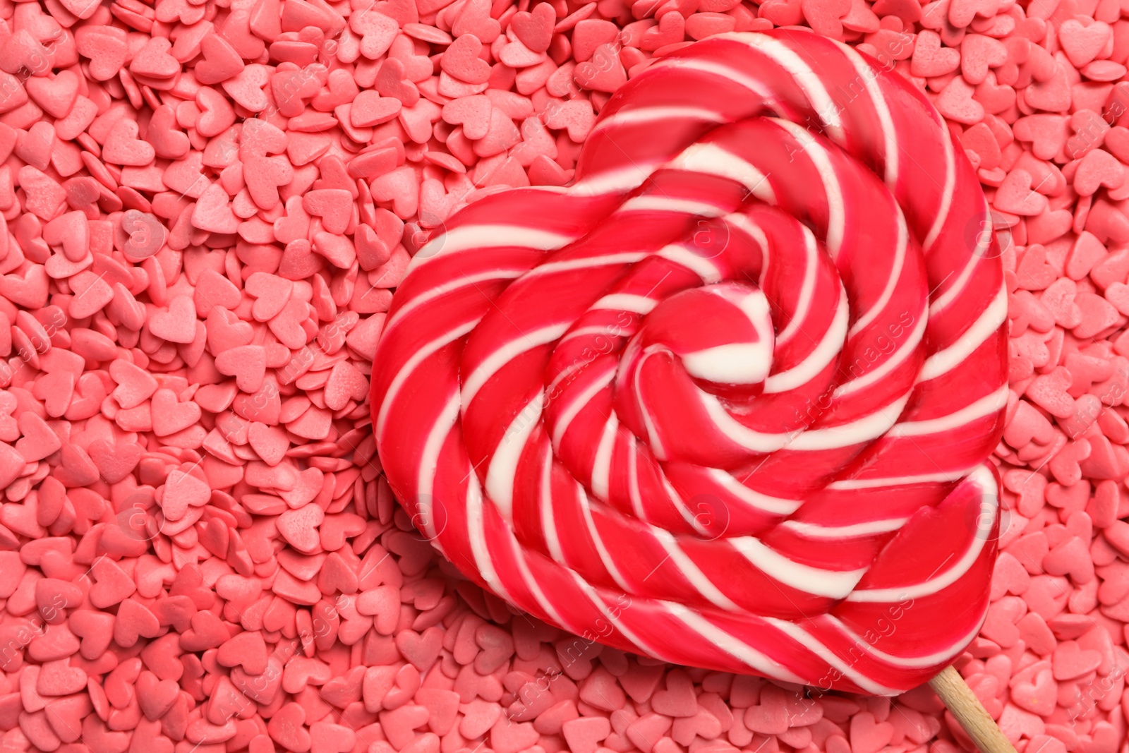 Photo of Sweet heart shaped lollipop on pink sprinkles as background, top view with space for text. Valentine's day celebration