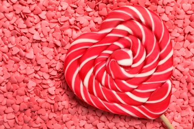 Sweet heart shaped lollipop on pink sprinkles as background, top view with space for text. Valentine's day celebration