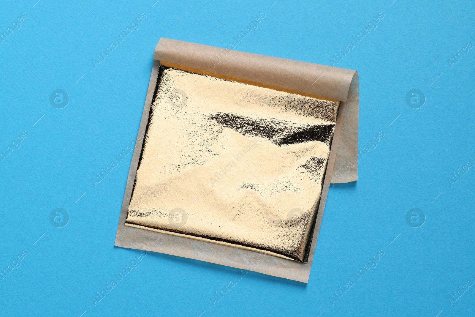 Photo of Edible gold leaf sheet on light blue background, top view