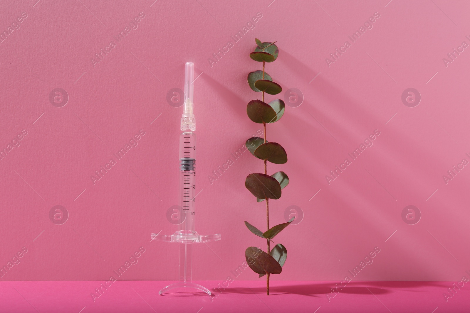 Photo of Cosmetology. Medical syringe and eucalyptus branch on pink background