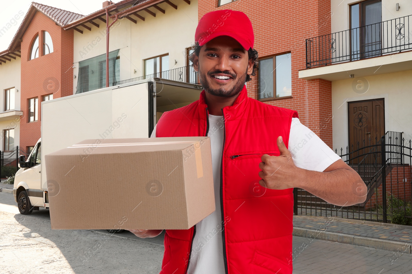 Image of Happy courier with parcel showing thumbs up outdoors