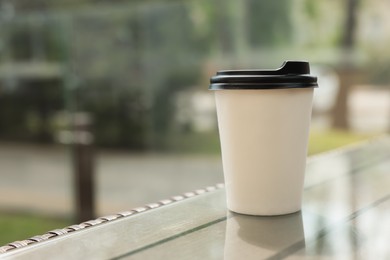 Photo of Paper takeaway cup on glass table outdoors. Coffee to go