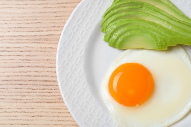 Photo of Plate of fried egg and avocado on wooden table, top view with space for text. Healthy breakfast