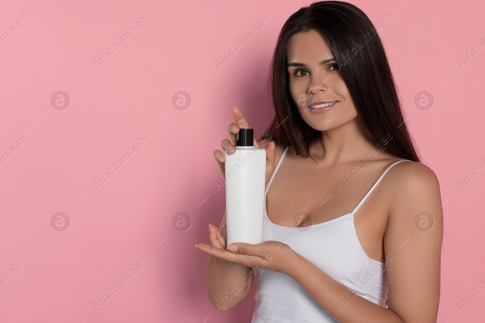 Photo of Beautiful young woman holding bottle of shampoo on pink background, space for text