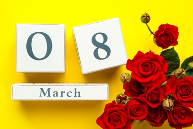 Photo of Wooden block calendar with date 8th of March and roses on yellow background, flat lay. International Women's Day