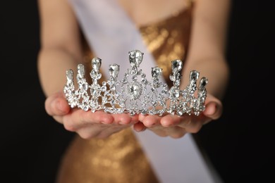 Woman in dress holding tiara on black background, closeup