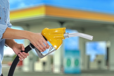 Image of Woman holding fuel nozzle near gas station, closeup