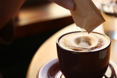 Woman adding sugar to aromatic coffee at table in cafe, closeup