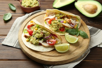Photo of Delicious tacos with guacamole, meat and vegetables served with lime on wooden table