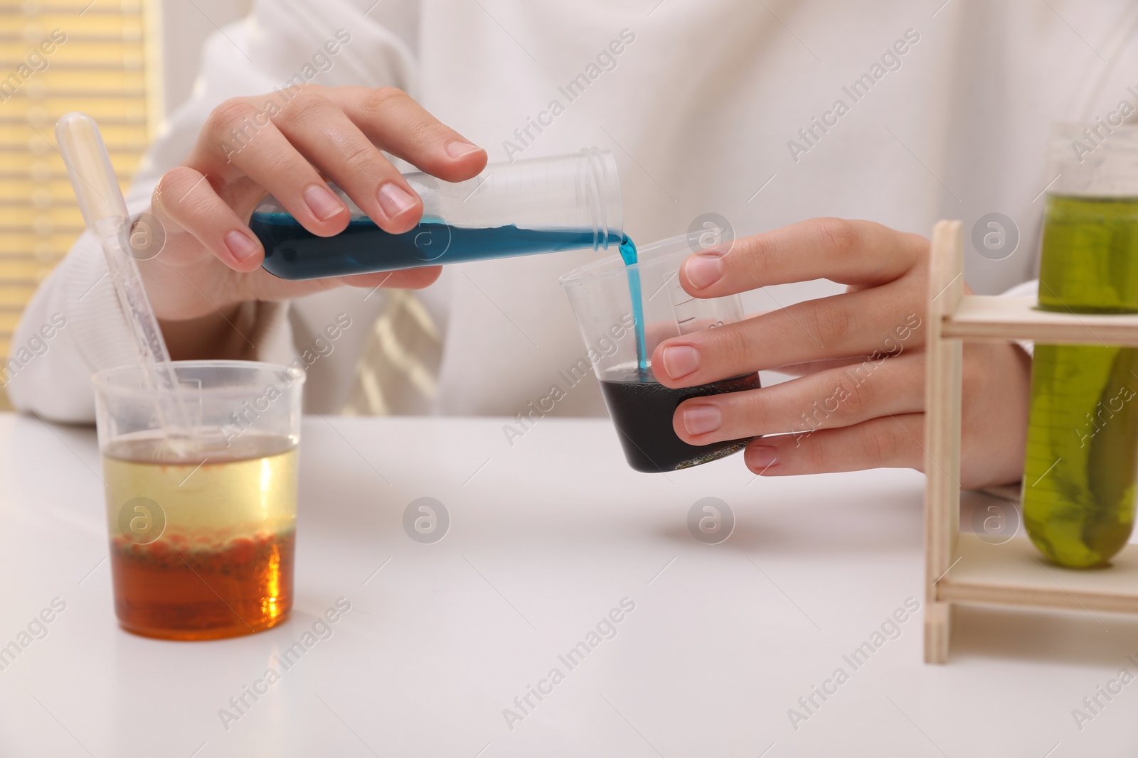 Photo of Girl mixing colorful liquids at white table indoors, closeup. Chemical experiment set for kids