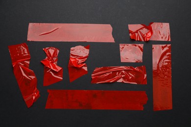 Photo of Many pieces of red adhesive tape on black background, flat lay