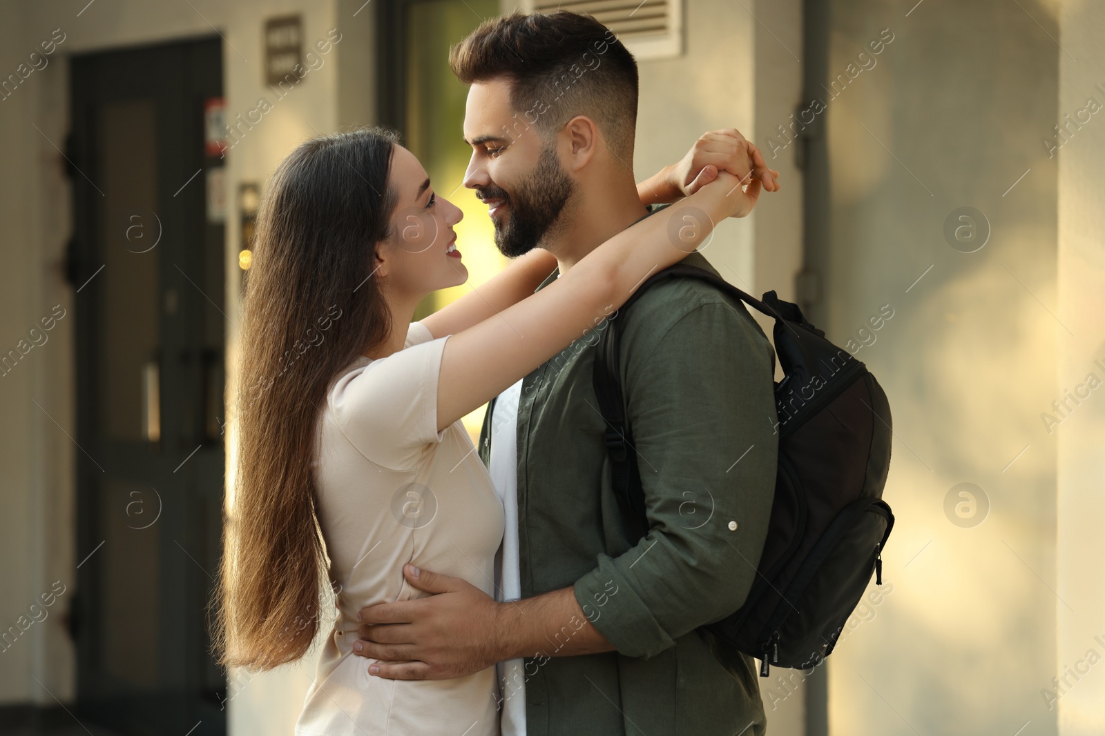 Photo of Long-distance relationship. Man with backpack hugging with his girlfriend near house entrance outdoors