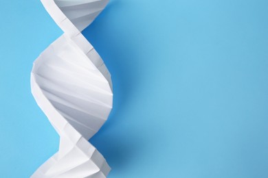 Photo of DNA molecule model madewhite paper on light blue background, top view. Space for text
