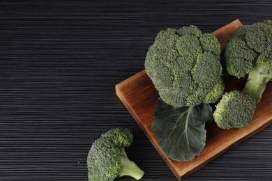 Photo of Board with fresh raw broccoli on black wooden table, above view. Space for text