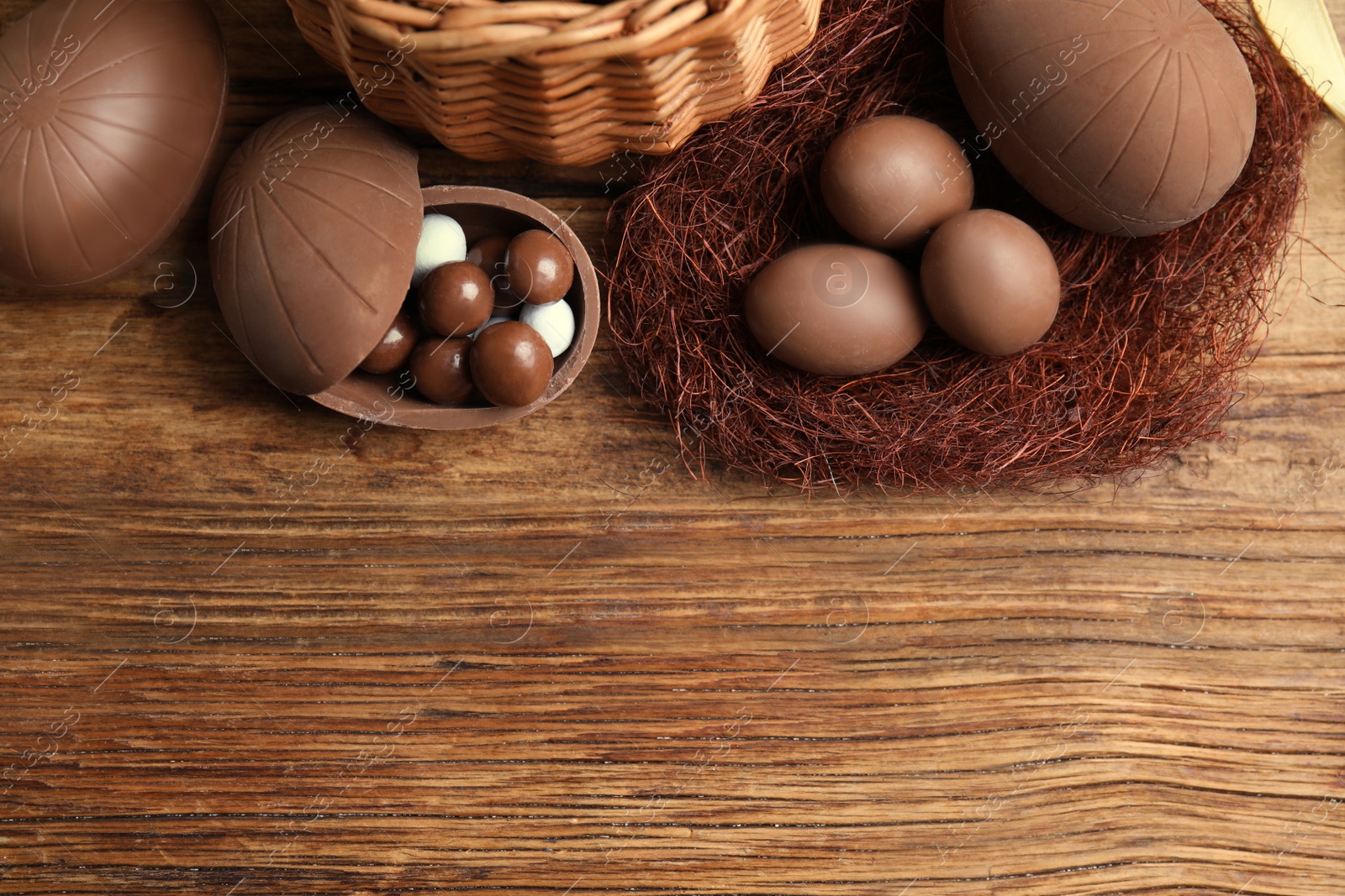 Photo of Flat lay composition with tasty chocolate eggs, wicker basket and decorative nest on wooden table. Space for text