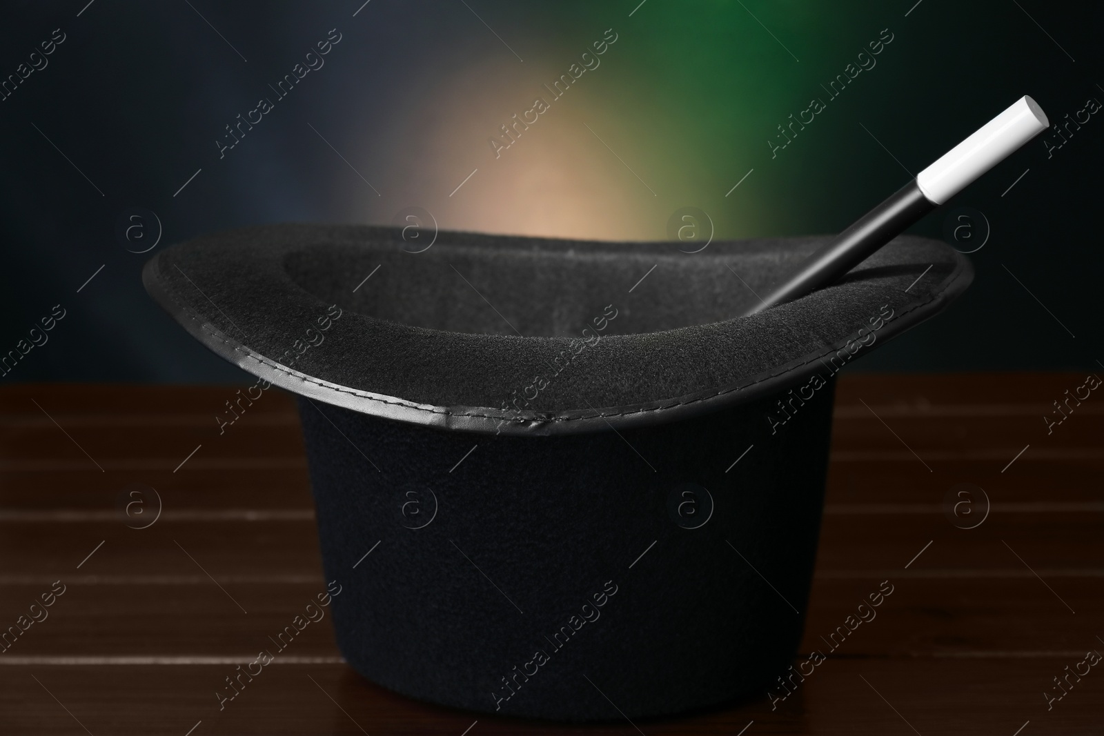Photo of Black top hat and wand on wooden table against color background, closeup. Magician equipment