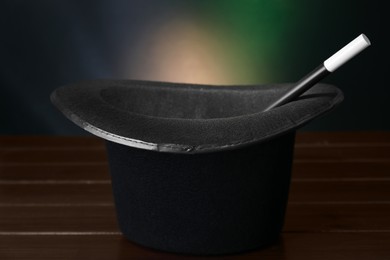 Black top hat and wand on wooden table against color background, closeup. Magician equipment