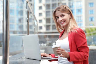 Photo of Beautiful businesswoman with laptop and cup of coffee on city street
