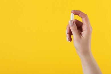 Photo of Woman holding vitamin pill on yellow background, space for text. Health supplement