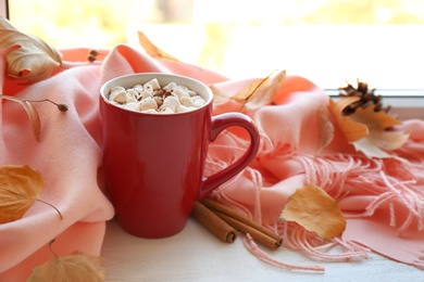 Photo of Cup of hot drink, scarf and autumn leaves on windowsill. Cozy atmosphere