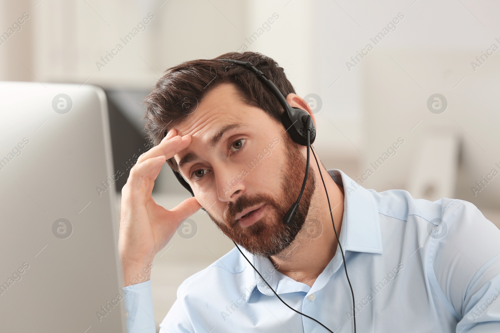 Photo of Tired hotline operator with headset working in office