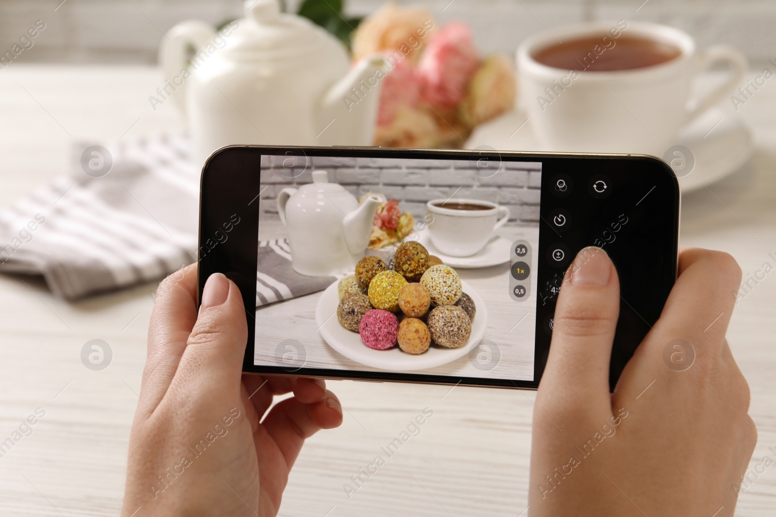 Photo of Blogger taking photo of tasty vegan candy balls at white wooden table, closeup