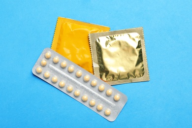 Photo of Condoms and birth control pills on light blue background, flat lay. Safe sex concept