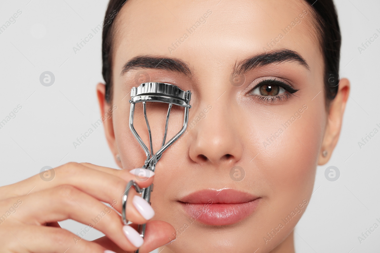 Photo of Beautiful young woman using eyelash curler on white background, closeup