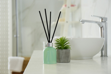 Photo of Reed air freshener and houseplant on counter in bathroom