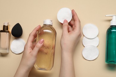 Woman with makeup remover, cotton pads, cosmetic product, sponge and foundation on beige background, top view