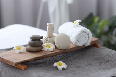 Stacked spa stones, flowers, herbal bags and towel on massage table indoors