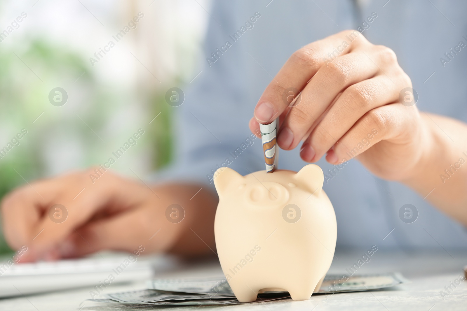 Photo of Woman putting money into piggy bank at table, closeup