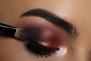 Photo of Applying dark eye shadow with brush onto woman's face, closeup. Beautiful evening makeup