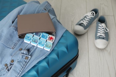 Photo of Suitcase with pill box and denim shirt on floor, closeup