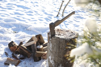 Metal axe in wooden log outdoors on sunny winter day