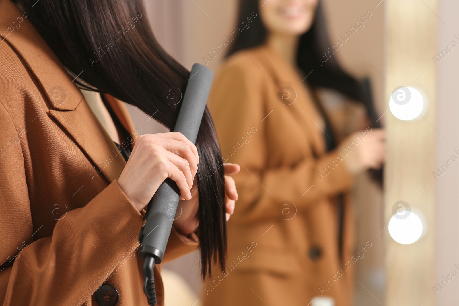 Photo of Woman using hair iron near mirror indoors, closeup. Space for text