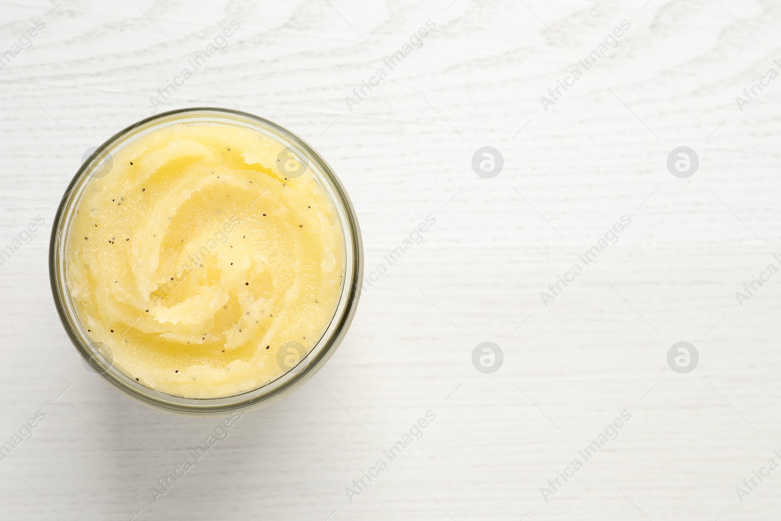 Photo of Body scrub in glass jar on white wooden table, top view. Space for text