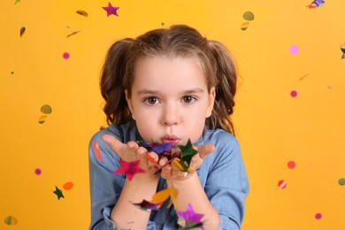 Photo of Adorable little girl blowing confetti on yellow background