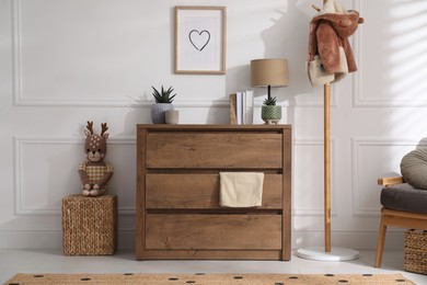 Stylish room interior with wooden chest of drawers near white wall