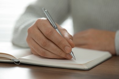 Photo of Man writing in notebook at wooden table, closeup