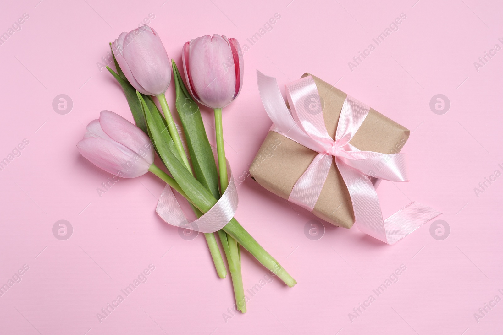 Photo of Beautiful gift box with bow and tulips on pink background, flat lay